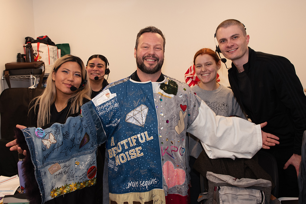 Quillon smiles posing in the Robe backstage, flanked by two stage managers on either side.