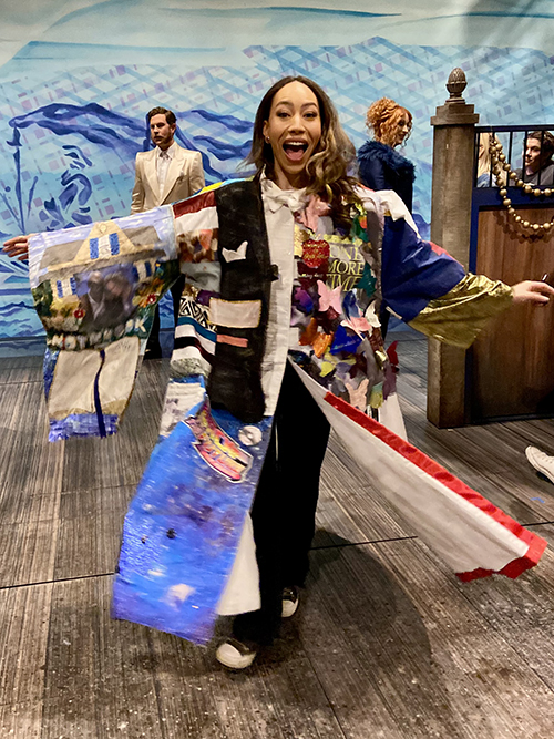 Hines stands in the Robe, her arms outstretched. The ground resembles the deck of the ship and the backdrop is nautical.