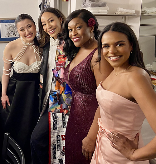 Hines stands backstage in the Robe in a group of four women wearing gowns. All are smiling.